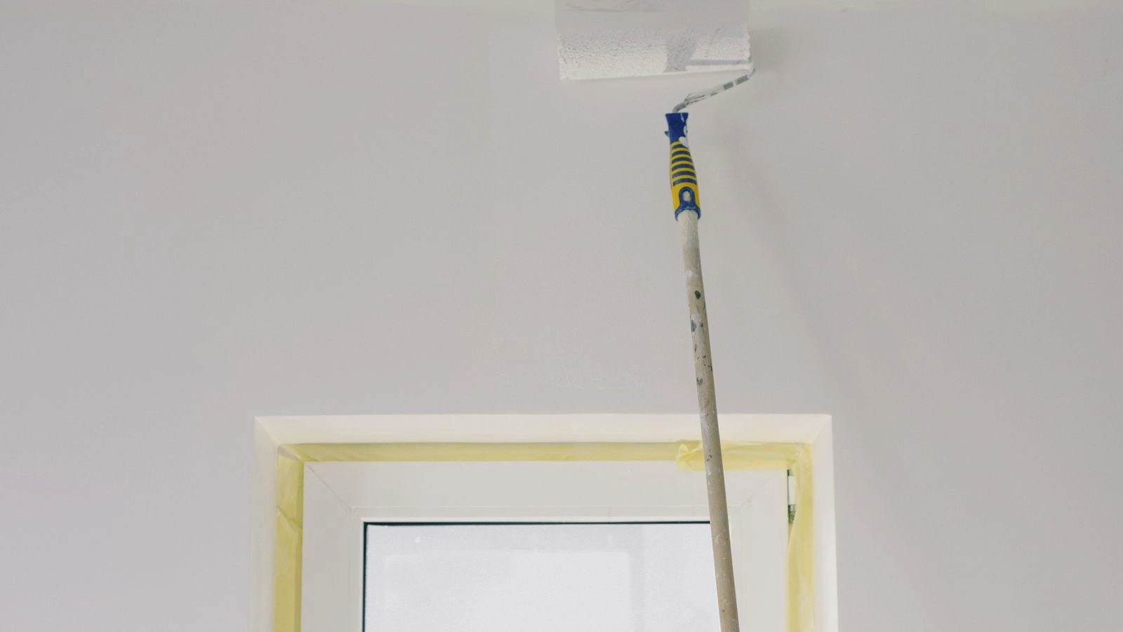 Rouleau sur perche appliquant une peinture blanche sur un plafond